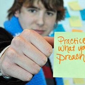 Soeren Palumbo holding up a post-it that reads: Practice what you preach.
