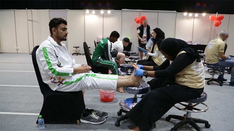 Athlete sitting in a chair receiving a foot examination by a health volunteer.