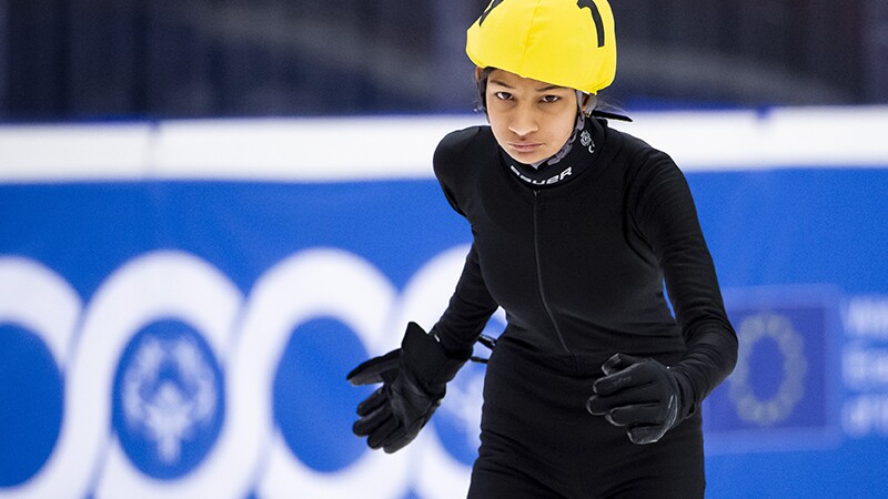 Speed Skater in all black with a yellow helmet preparing to skate.