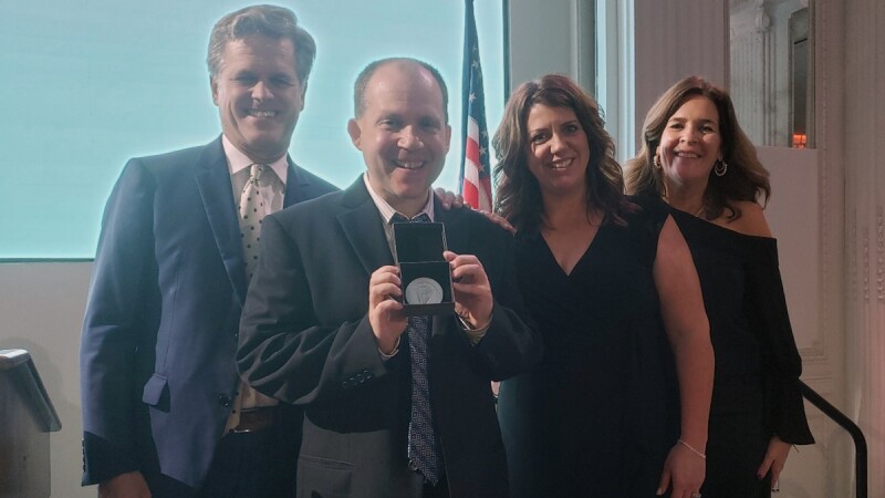 Four people side by side, a man is showing an award. 