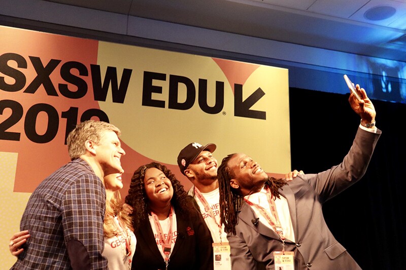 Small group of athletes and Special Olympics representatives pose for group selfie taken by Jamaal Charles in front of the SXSW EDU 2019 sign.
