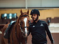 a man in an equestrian outfit standing next to a horse and holding the reins. 