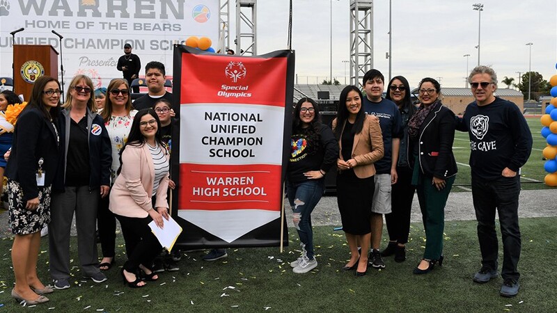 School representatives and unified teams standing by a national unified champion school banner. 