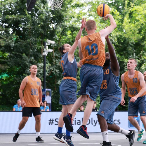 A group of basketball players in grey and orange vie for the ball on a basketball court. 