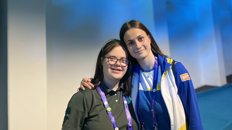 Dos atletas de pie uno al lado del otro, sonriendo y con los brazos alrededor de los hombros de la otra.