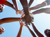 a group of athletes standing in a circle putting their hands in the middle, one on top of the other. 