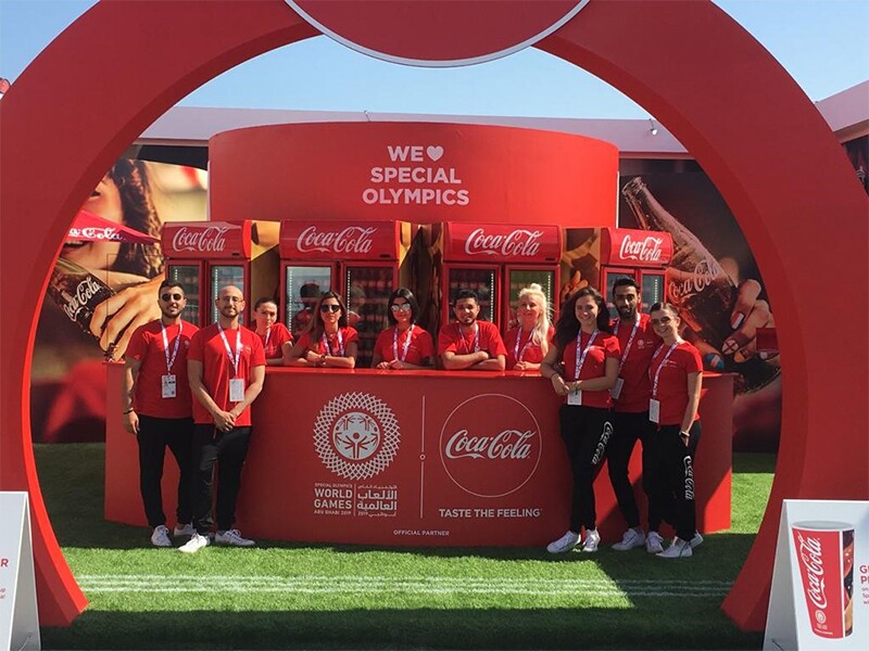 Coca Cola representatives standing at the Coca Cola booth in Abu Dhabi at the summer games.