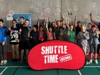 A group of more than 20 participants standing together, raising their badminton rackets, behind a banner with “Shuttle Time” Oceania. 