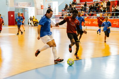 Football match with a player in a blue jersey entering the penalty area to shoot, while a player in a red shirt attempts to block him.