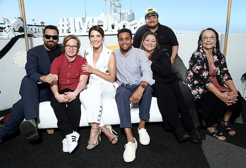 The cast of Stumptown sitting together in a group on a white couch.