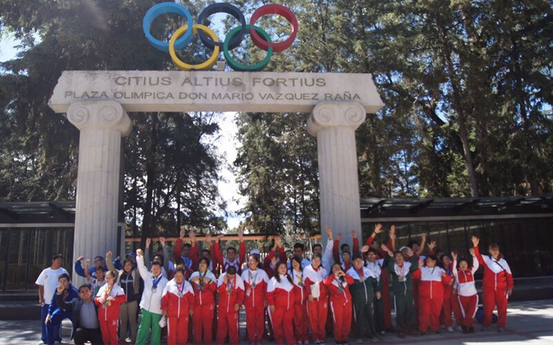 Group of athletes and representatives standing under columns that are holding up the Olympics rings.