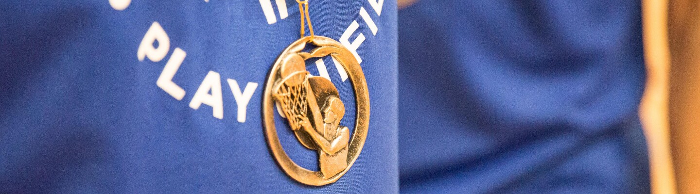 Athlete with a blue Play Unified shirt on and a gold European Basketball medal hanging down.