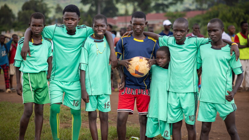 A team of young boys standing side by side on a field with their arms around one another's shoulders. 
