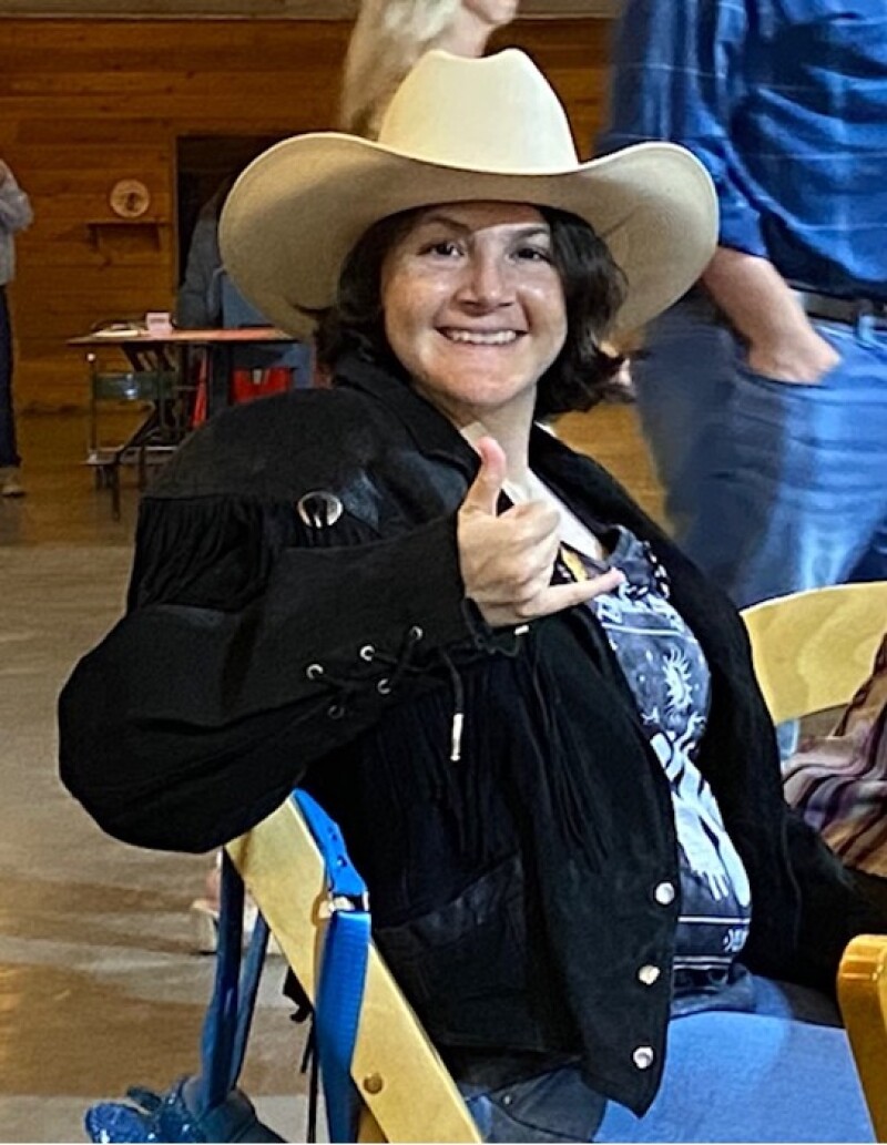 A woman wearing a cowboy hat gives a thumbs up to the camera.