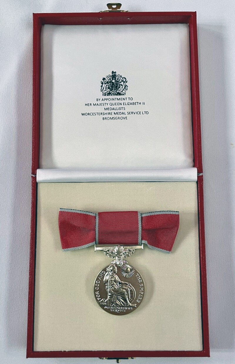 The British Empire medal in it’s case with a message written at the top that says “BY APPOINTMENT TO HER MAJESTY QUEEN ELIZABETH II MEDALLISTS WORCESTERSCHIRE MEDAL SERVICE LTD BROMSGROVE.”
