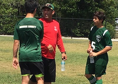 Coach Pedro with two athletes on the field.