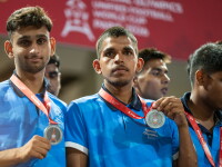 Two athletes in blue team jerseys hold up silver medals while standing together during a medal ceremony.