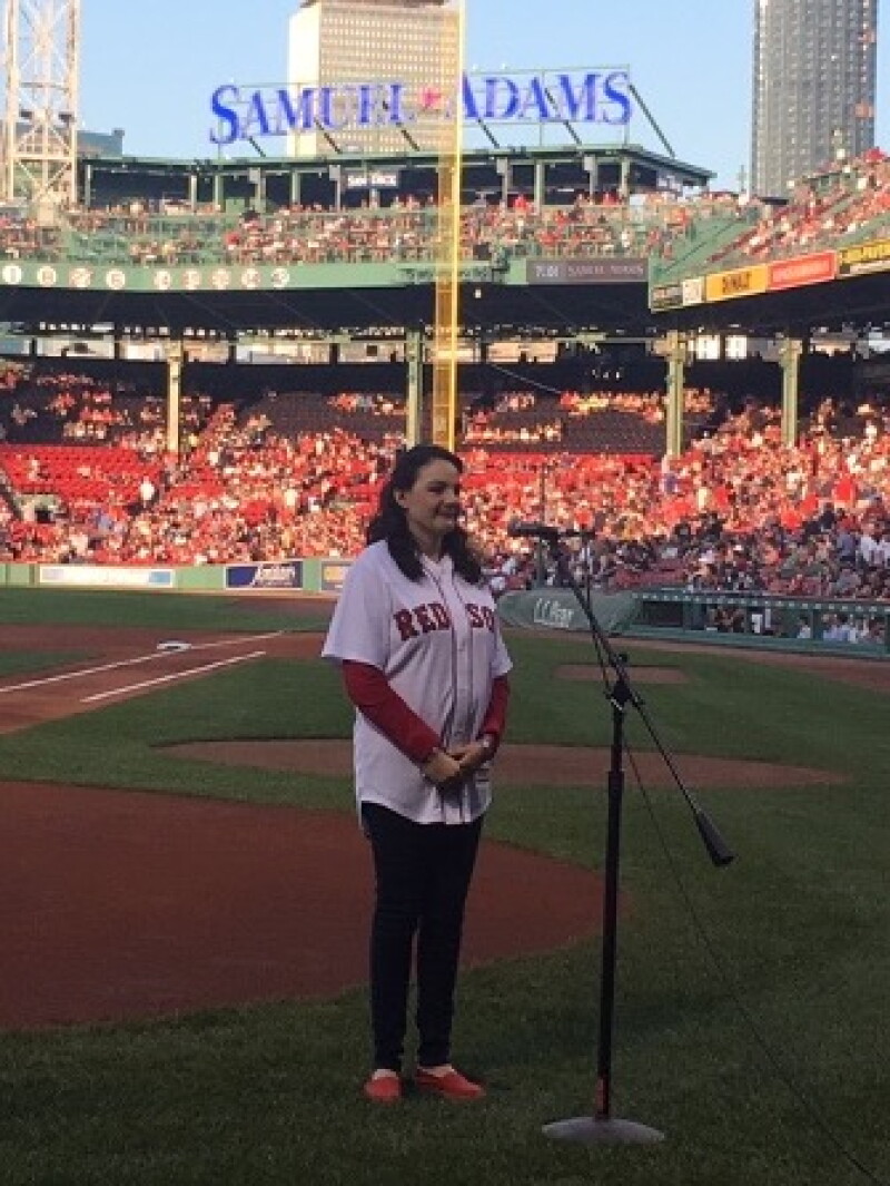 A woman stands on a baseball field behind a microphone.
