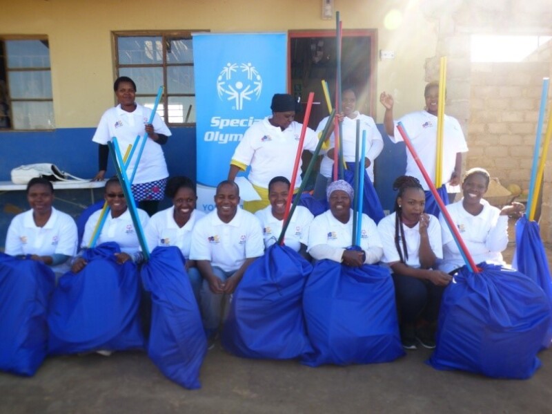 A group of coaches sit for a group photo in front of a blue Special Olympics banner. 