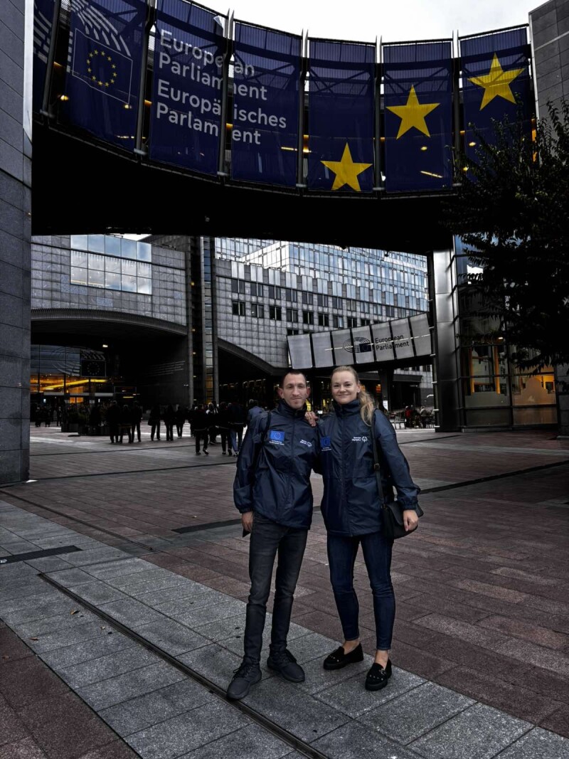Two individuals stand outside of a building for a photo.