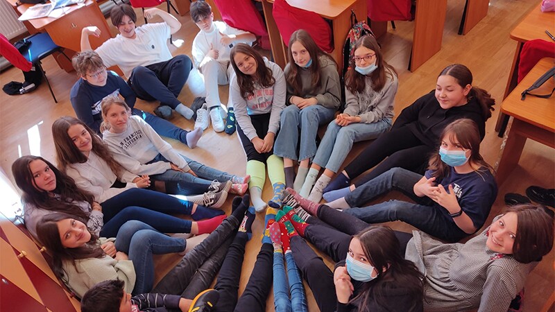 A group of students sitting in a circle with their feet together and showing off their socks. 