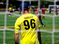 A Special Olympics athlete wearing a yellow goalie jersey stands in the soccer net, facing the field. 