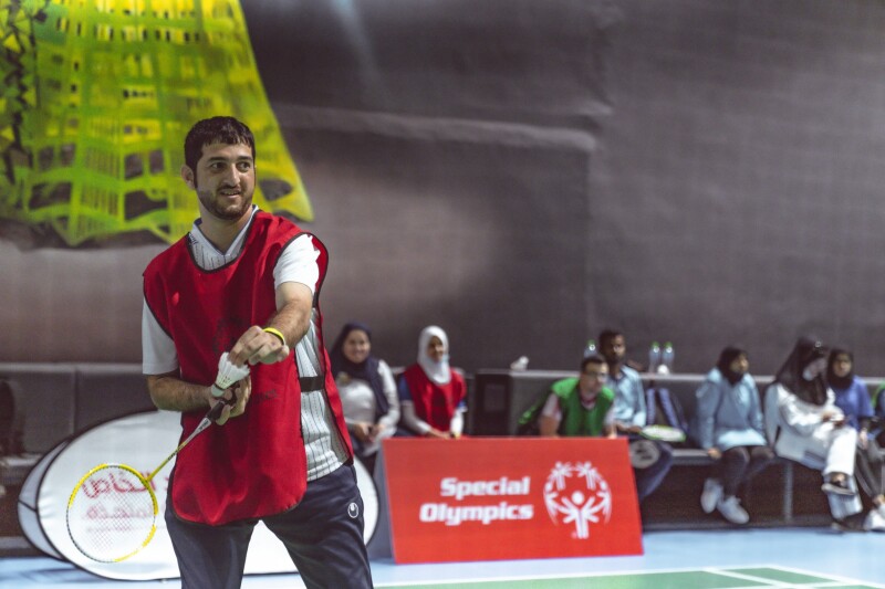 An athlete stands near the back of the court holding out racket and Shuttlecock preparing to serve over the next