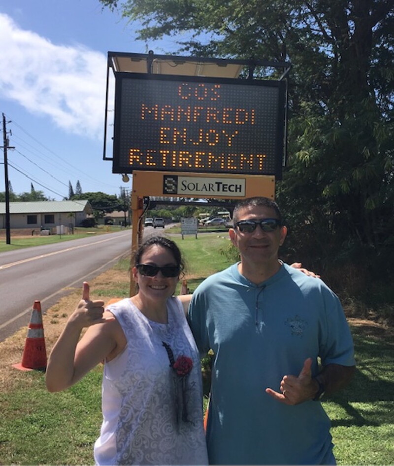 Two people stand in front of an electronic sign. They are smiling for the camera.