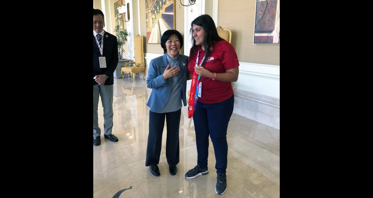 An adult and young adult standing in a hall way talking and laughing.