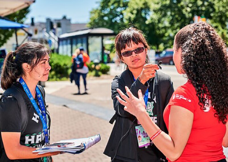 Two young women use a microphone to interview another woman.