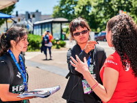 Two young women use a microphone to interview another woman.