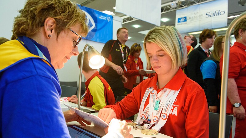 Daina Shilts sitting at a desk with her medals around her neck reading over a card with a health representative.