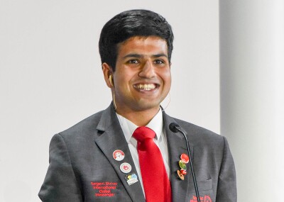 Haseeb Abasi staing on stage in his gray Sargent Shriver International Global messenger blazer and red tie.