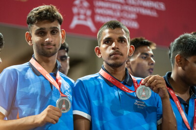 Dos atletas con camisetas azules de sus equipos levantan medallas de plata mientras permanecen juntos durante una ceremonia de entrega de medallas.