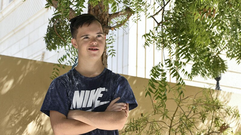 Briton outside under a tree smiling and looking up.