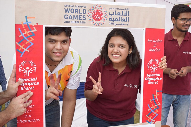 Athlete and volunteer standing behind a decorative fraom from the Special Olympics World Games Abu Dhabi 2019 posing together for a photo.