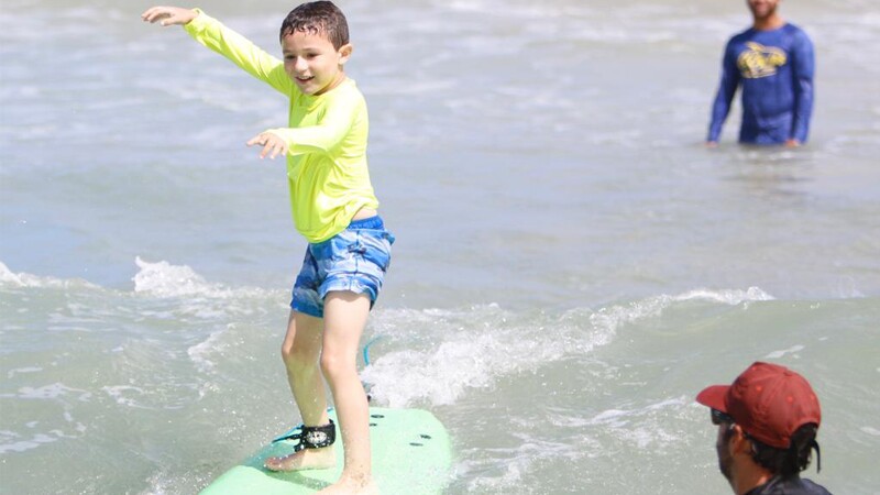 Young boy surfing with two observers watching.