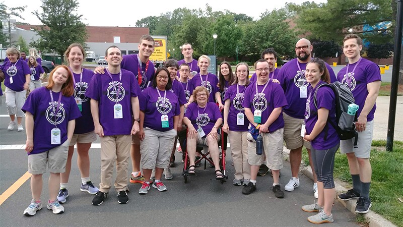 Special Olympics Hamilton swim team of 17 people in purple shirts standing outside for a group photo.
