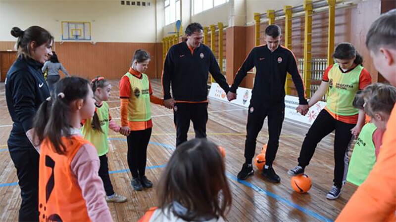 Footballers and athletes standing in a circle holding hands.