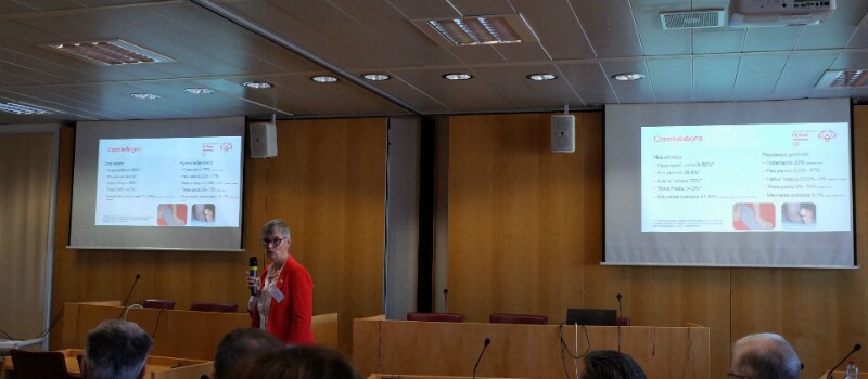 Female speaker with a microphone presents powerpoint presentation at the top of a room.