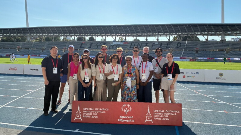 Group of people standing on a track with Unified Football World Cup Paris 2026 signage in front of them with the field in the background. 