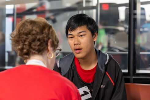 Young man speaking while a woman looks down and appears to be taking notes. 