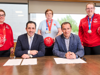 SOEE and TME representatives signing the agreement while Special Olympics athletes hold footballs