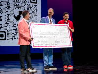 Three people holding a large-sized check while standing on a stage.