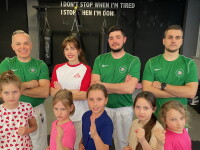 A group of four men and one woman stand behind a group of five girls holding karate poses.