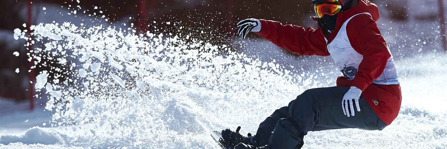 Snowboarder in a red ski jacket and gray ski pants performing moves in the snow.