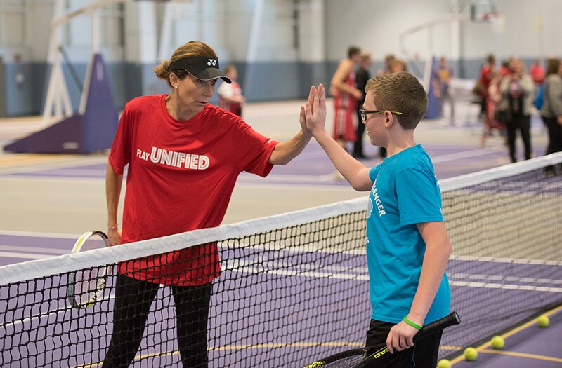 Two tennis players give one another high-5 over tennis net.