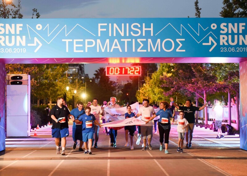 A group of people run towards the camera and across a finish line holding banners and waving their arms in the air.