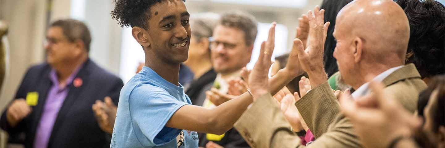 Student giving high-5s to adults that are standing in a line.