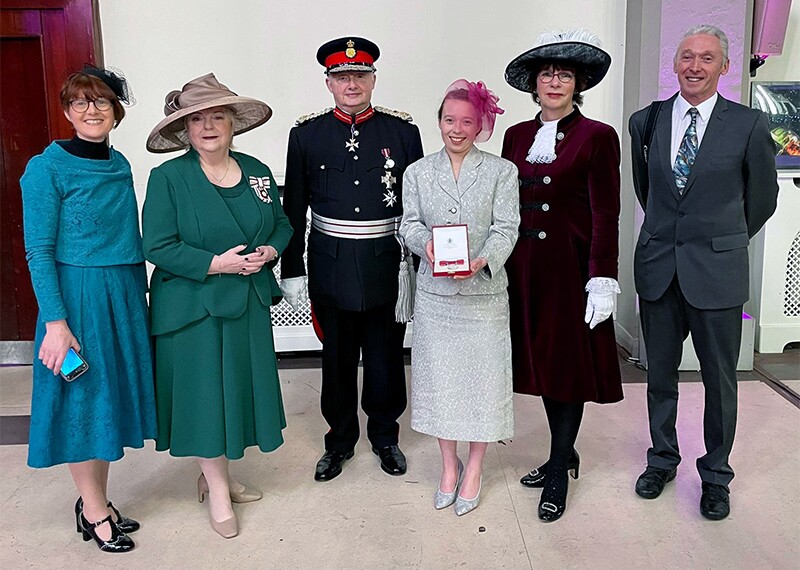 Kiera holding the British Empire Medal, smiling next to the lord-lieutenant, the High Sheriff, and members of Kiera's family.